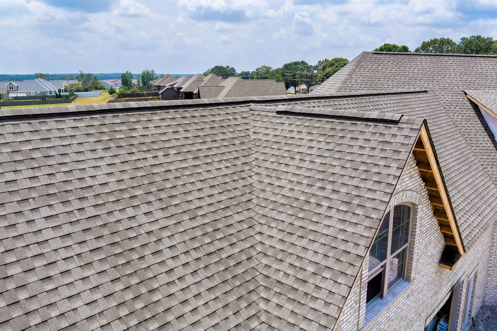 New roofing installation on residential houses under cloudy sky in suburban area with green surroundings